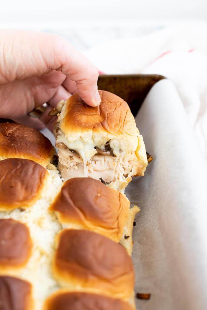hand grabbing a sandwich from a tray of deli turkey roll sliders 